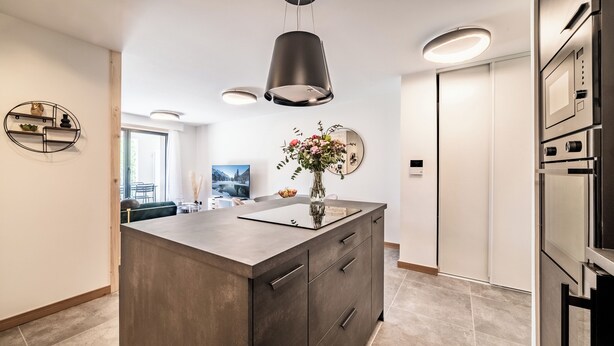 A modern kitchen with a central island, built-in appliances, and a dining area visible through an open door.