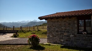 A stone building with a tiled roof, a gravel path, and a flower bush. - Les Xanes: El Trasgu - mountain views, terrace, and Wi-Fi (Cangas de Onís)