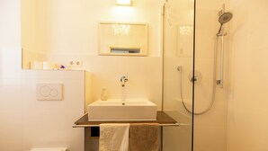 Ein modernes Badezimmer mit einer gläsernen Duschkabine, einem weißen Waschbecken und einer Toilette.
