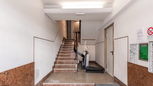 Eine Treppe führt zu einer oberen Etage, mit einer Handlauf auf einer Seite und einer Tür auf der anderen.