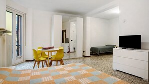 Ein Zimmer mit Schachbrettmuster-Boden, einem Bett, einem Fernseher auf einer Kommode, einem Esstisch mit Stühlen und einer Tür zu einem anderen Raum.