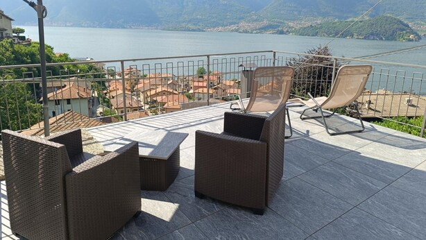 A terrace with wicker furniture, a large umbrella, and a view of a lake and mountains. - Apartment 'Dudi Jolie' with Lake View, Whirlpool, Terrace and Wi-Fi (Lezzeno)