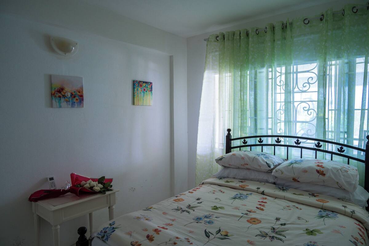 A bedroom with a bed, a bedside table, and a window with curtains.