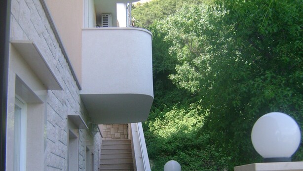Un étroit couloir extérieur avec un escalier menant à un balcon.