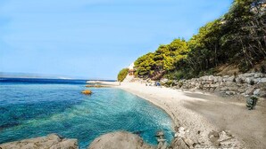 Une plage côtière aux eaux turquoise et limpides, avec un rivage rocheux et quelques personnes visibles au loin.