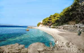 Een kuststrand met helder turquoise water, een rotsachtige kustlijn en enkele mensen in de verte.