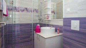 A modern bathroom with a glass shower enclosure, a white sink with a pink soap dispenser, and a purple tiled floor. - Sea ViewApartments Lendic Podgora- Superior Studio (Podgora)
