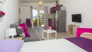 A modern hotel room with a bed, a sofa, a small table, a TV, a kitchen area, and a balcony with a view. - Sea ViewApartments Lendic Podgora- Superior Studio (Podgora)