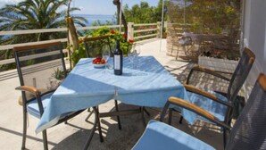 An outdoor patio with a table set for two, covered by a blue tablecloth, surrounded by wicker chairs. - Sea ViewApartments Lendic Podgora- Superior Studio (Podgora)