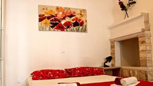 A hotel room with a bed, a fireplace, a painting of flowers, and a red bedspread.