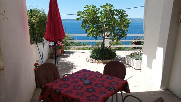 A balcony with a table and chairs, a red umbrella, and a view of the sea.