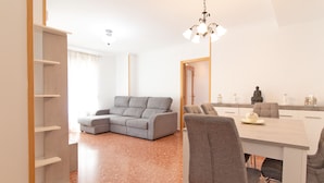 A modern living room with a grey sectional sofa, a dining table with four chairs, and a chandelier.