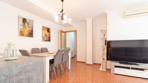 A modern living room with a dining area, a flat-screen TV, and artwork on the walls.
