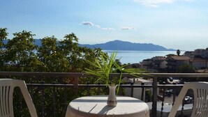 Ein Balkon mit Tisch, einer Topfpflanze und Blick auf das Meer und die Berge.