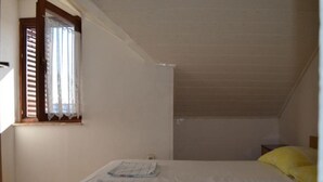 Ein kleines Zimmer mit einem Einzelbett, schrägen Wänden und einem Fenster mit Holzhörnern.