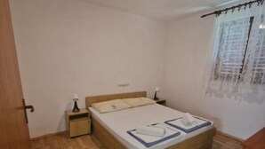 Un dormitorio con una cama de madera, dos mesitas de noche y un ventanal con cortinas de gasa.
