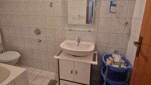 A bathroom with a white sink, mirror, and toilet. There is a blue trash bin next to the sink.