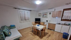 A compact living space with a dining table, chairs, a sofa, a TV, a microwave, and a small kitchenette.