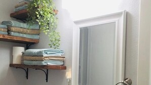 A bathroom with a white sink, a mirror, a towel rack, and a shelf with folded towels.