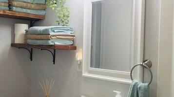 A bathroom with a white sink, a mirror, a towel rack, and a shelf with folded towels.