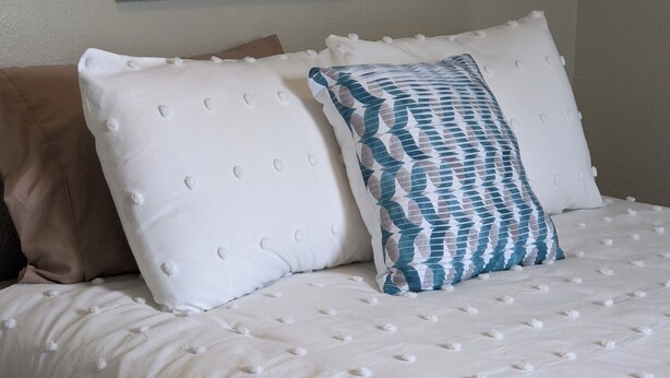 Una cama con ropa de cama blanca y dos almohadas, una lisa y otra con estampado azul.
