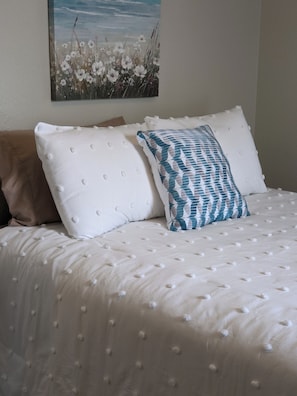 A bed with white bedding and two pillows, one plain and one with a blue pattern. - Charming 2-bedroom house in Hutchinson with WiFi and AC (Hutchinson)