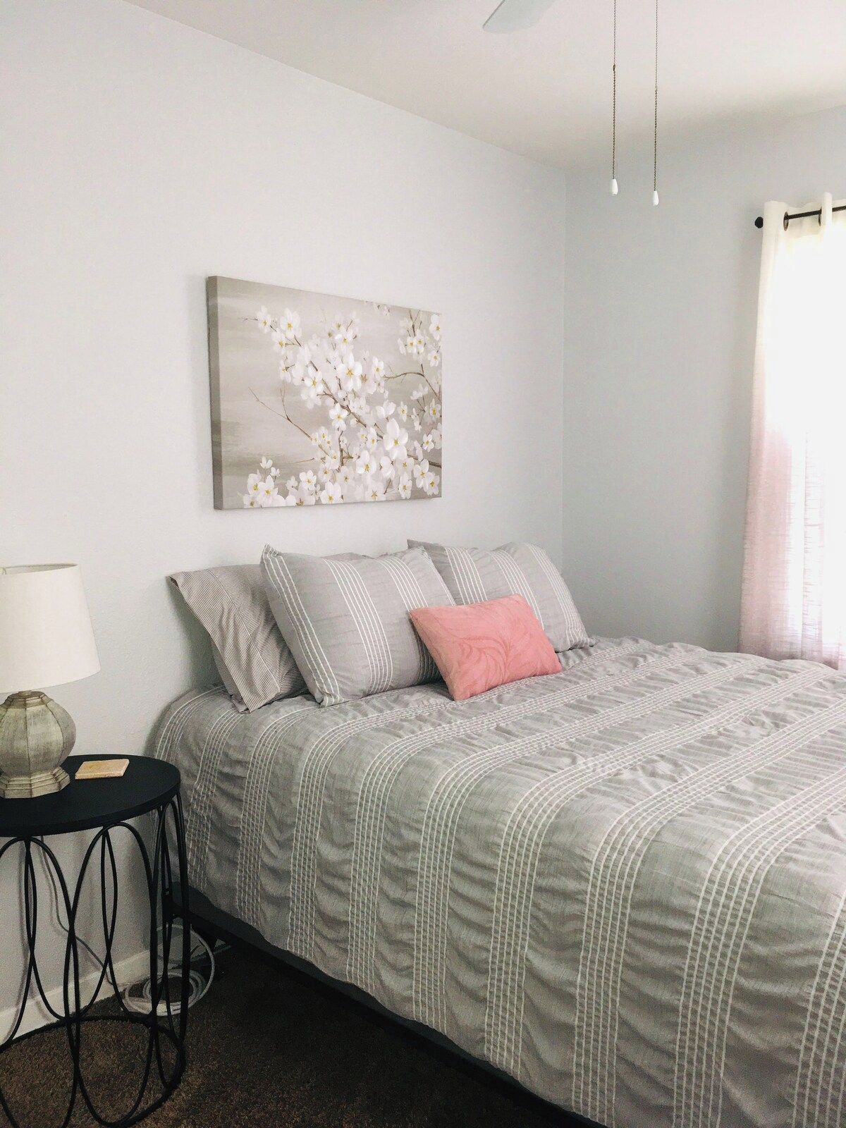 A bedroom with a bed, pillows, a bedside table, a lamp, and a wall-mounted artwork.