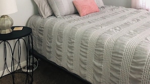 A bedroom with a bed, pillows, a bedside table, a lamp, and a wall-mounted artwork.