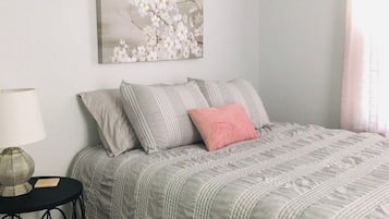 A bedroom with a bed, pillows, a bedside table, a lamp, and a wall-mounted artwork.