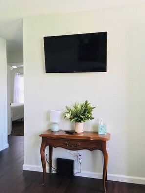 A room with a mounted TV, a wooden console table with a plant, a lamp, and a tissue box. - Park View Cottage Near Carey Park (Hutchinson)