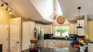 A modern kitchen with white cabinets, a central island, stainless steel appliances, and a chandelier. - River front paradise,  boat, kayak, swim,  go to the racetrack, have fun, relax! (Cayuga)