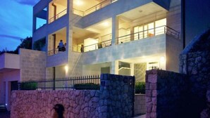 Un moderno edificio de varios pisos con fachada de piedra, varios balcones y una escalera que conduce a la entrada.