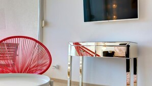 Ein modernes Zimmer mit weißer Wand, einem Fernseher über einem metallischen Konsolentisch und einem roten Sessel.