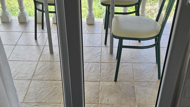 Une vue à travers une porte vitrée donnant sur un patio extérieur, avec un sol carrelé et du mobilier de jardin.