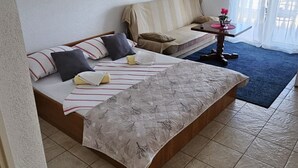 Une chambre à coucher avec un lit, un canapé, une petite table et une fenêtre avec des rideaux.