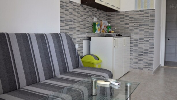 Eine moderne Küche mit einem gestreiften Sofa, einem Glastisch mit Fernbedienungen und einem kleinen Kühlschrank.