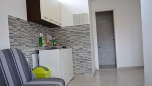 Ein kompakter Wohnraum mit einer Couch, einem kleinen Tisch, einem Kühlschrank und einer Tür mit der Aufschrift 'Home'.