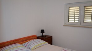 Ein Schlafzimmer mit Bett, Kissen, einem Nachttisch mit Lampe und einem Fenster mit Jalousien.