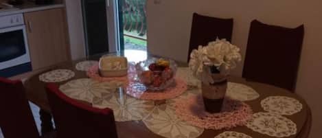A dining table with lace doilies, a vase with flowers, and a bowl of fruit.