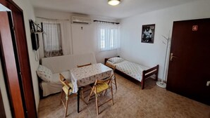 Une petite pièce, de taille modeste, comprenant un lit simple, un canapé, une table avec des chaises et une fenêtre avec des rideaux.