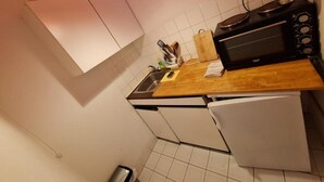 Une cuisine compacte avec des meubles blancs, un plan de travail en bois, un micro-ondes noir et un petit réfrigérateur.