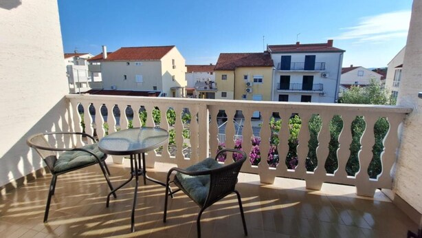Un balcon avec une table et deux chaises, une balustrade avec des panneaux de verre et des bâtiments en arrière-plan.