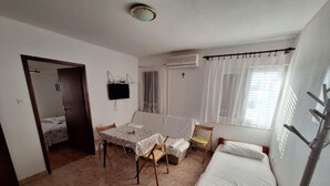 Une petite pièce propre, avec un lit, une table et des chaises, un téléviseur et une fenêtre avec des rideaux.