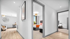 Una habitación de hotel moderna con piso de madera, una cama con ropa de cama naranja, un escritorio con una silla y un ventanal con vistas al exterior.