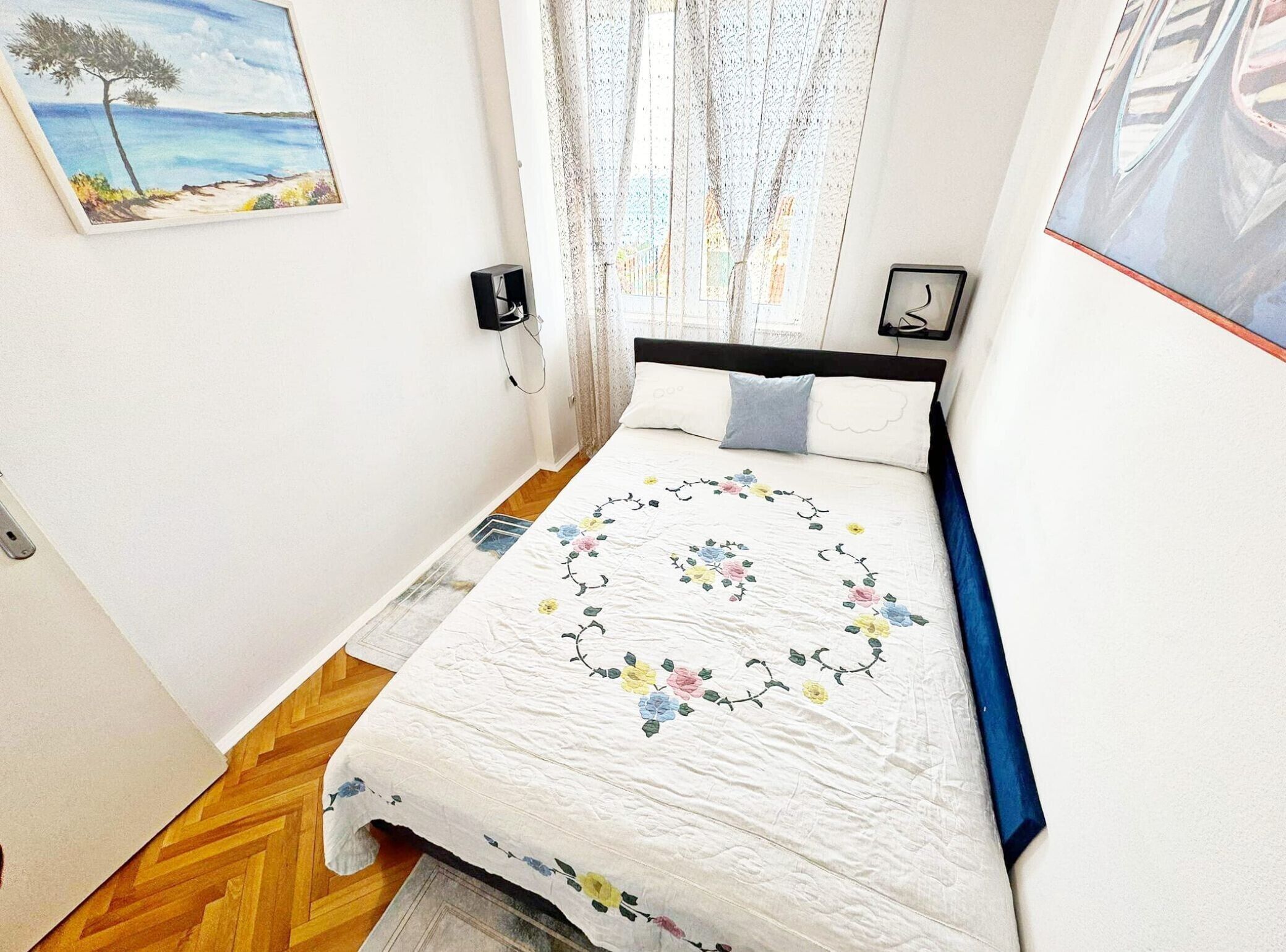 A bedroom with a bed, a painting, a window with curtains, and a wall-mounted phone.