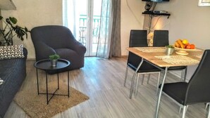 A modern living room with a sofa, a small table with a plant, a dining table with chairs, a TV, and a balcony view. - Apartments Silva - Superior Two Bedroom Apartment with Balcony and Sea View (Slatine)