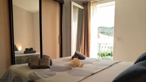 A hotel room with a bed, towels, a mirror, and a view of the outdoors. - Apartments Silva - Superior Two Bedroom Apartment with Balcony and Sea View (Slatine)