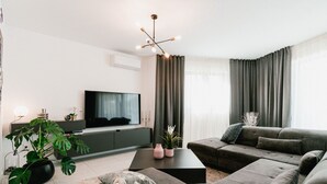 A modern living room with a grey sofa set, a flat-screen TV, a coffee table, and a potted plant.