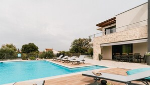 A modern outdoor pool area with lounge chairs and a table, surrounded by a stone building with a balcony.