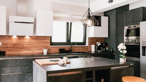A modern kitchen with dark cabinetry, a central island, wooden stools, and a hanging light fixture.